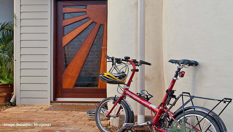 A home's paved front porch with a decorative sunburst pattern on the front door, and a bicycle propped against the wall.
